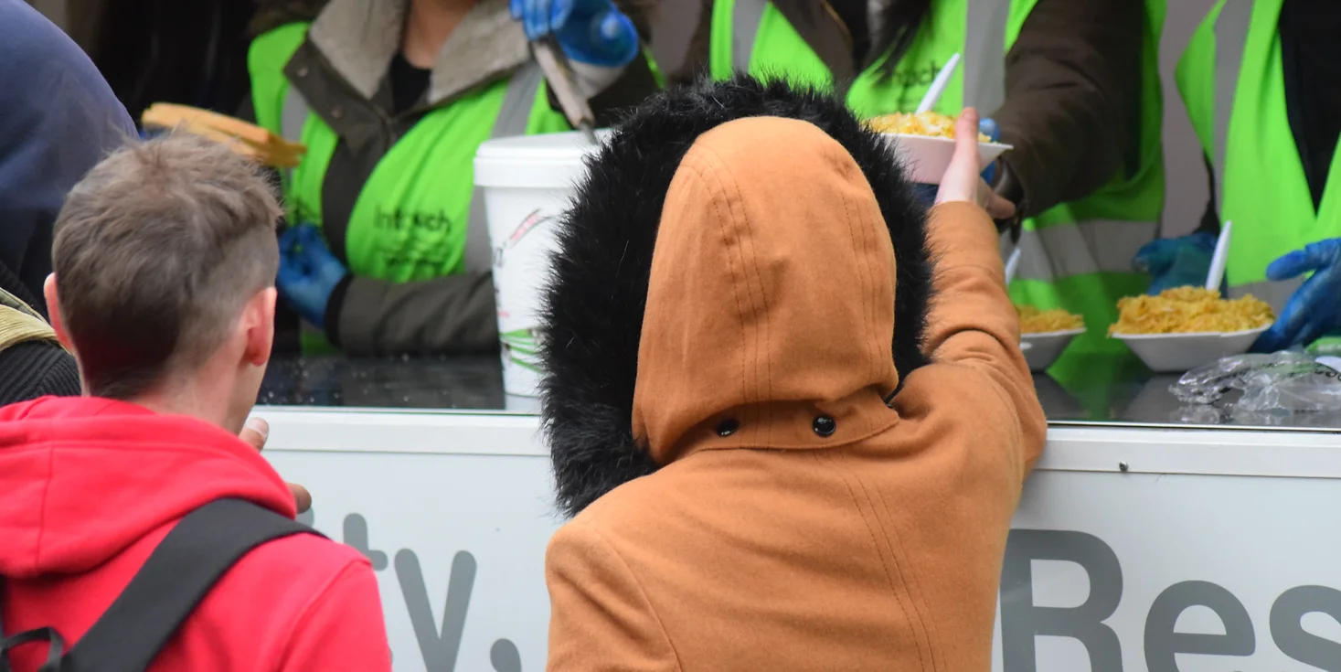 A child in a winter coat, facing away from the camera, is being handed food from a mobile kitchen